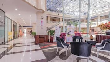 A spacious atrium with a high ceiling and a glass roof, featuring a reception desk, seating area, and a staircase leading to upper levels.