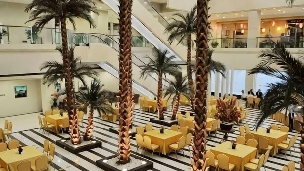 A hotel lobby with multiple dining areas, palm trees, and an escalator. - Zhong Ji Subaru Hotel (BEIJING)