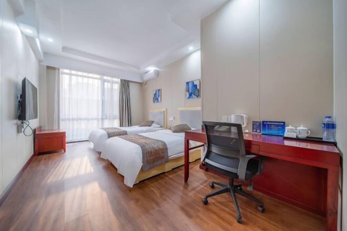 Habitación de hotel con dos camas, un escritorio, una silla, un televisor y obras de arte en las paredes.
