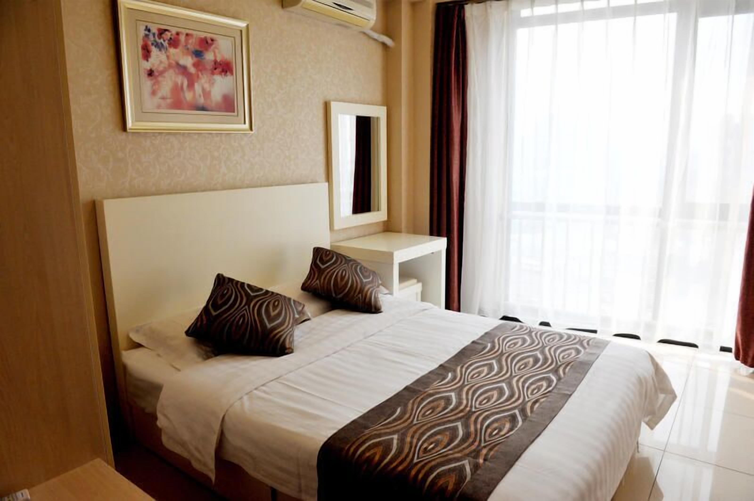 A hotel room with a large bed, a bedside table with a mirror, and a window with curtains.
