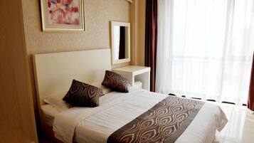 A hotel room with a large bed, a bedside table with a mirror, and a window with curtains.