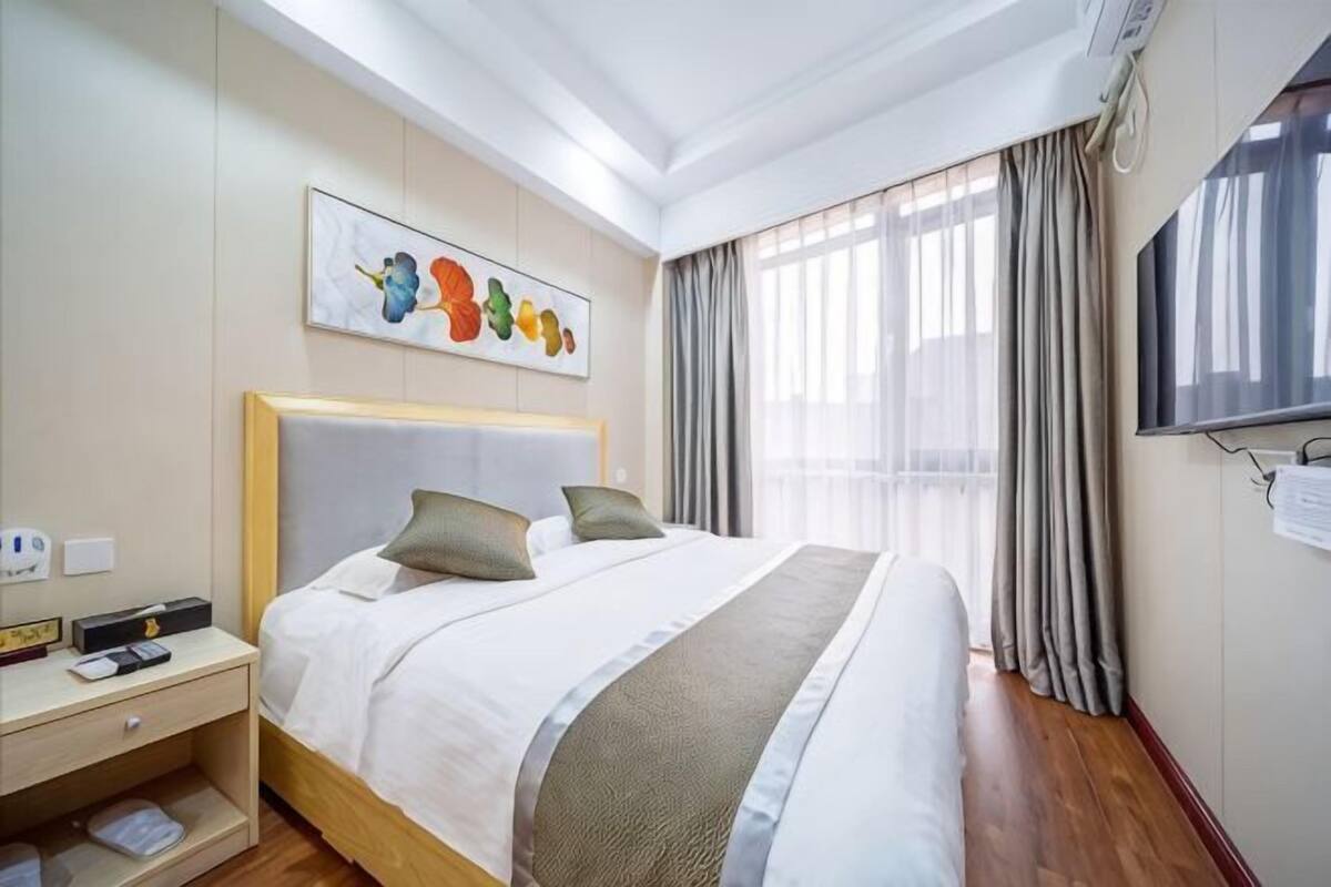 Habitación de hotel con cama, mesita de noche, televisor y ventana con cortinas.
