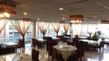 Un restaurante con mesas redondas, sillas y candelabros colgantes.