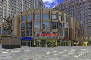 A hotel with a central entrance, a statue in front, and multiple floors visible in the background.