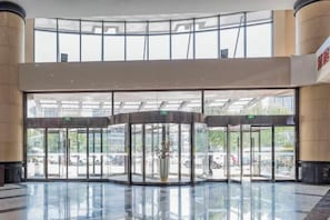 Um hall de entrada com porta giratória, paredes de vidro e piso espelhado.