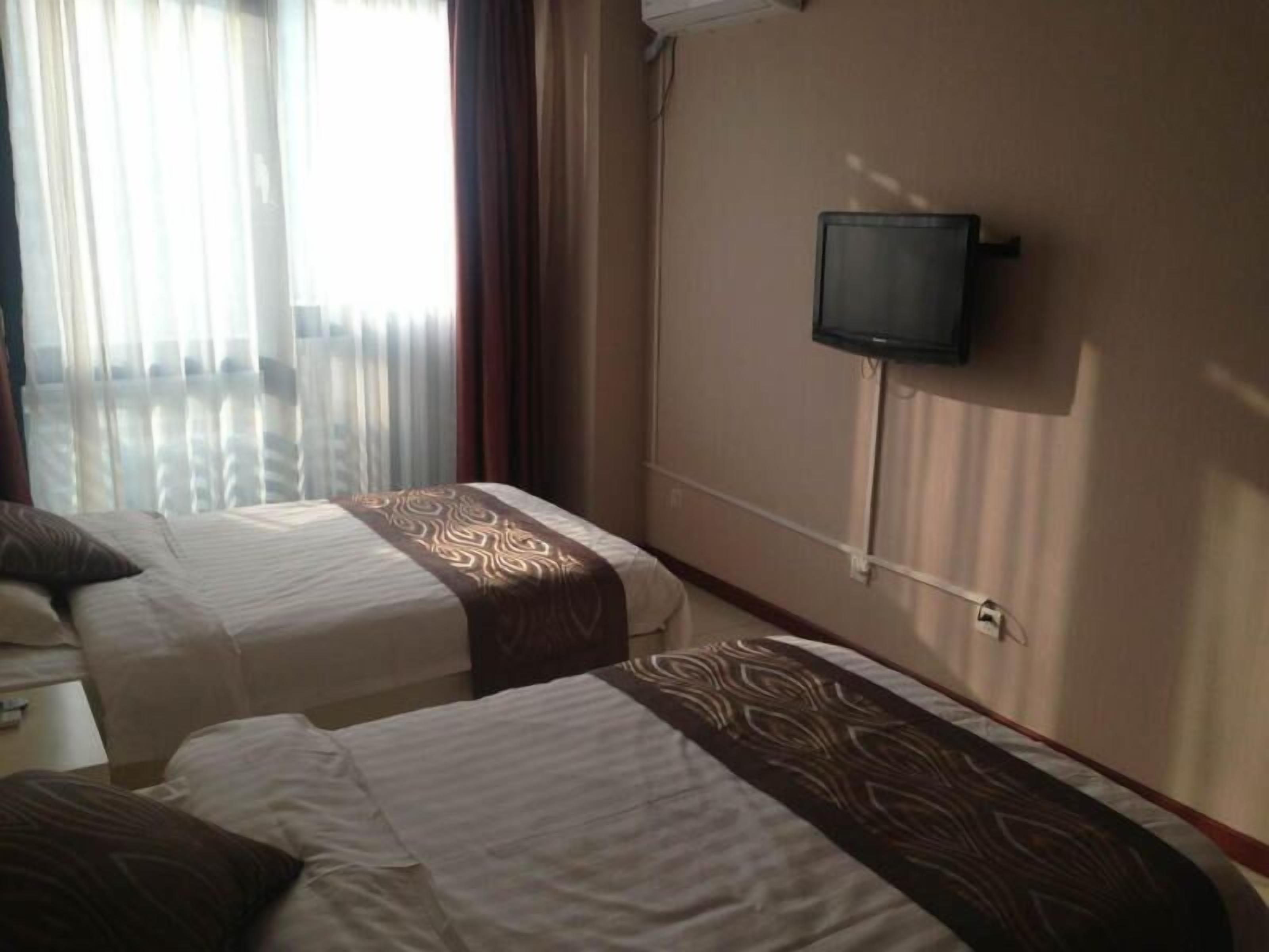 A hotel room with two beds, a TV on the wall, and a window with curtains.