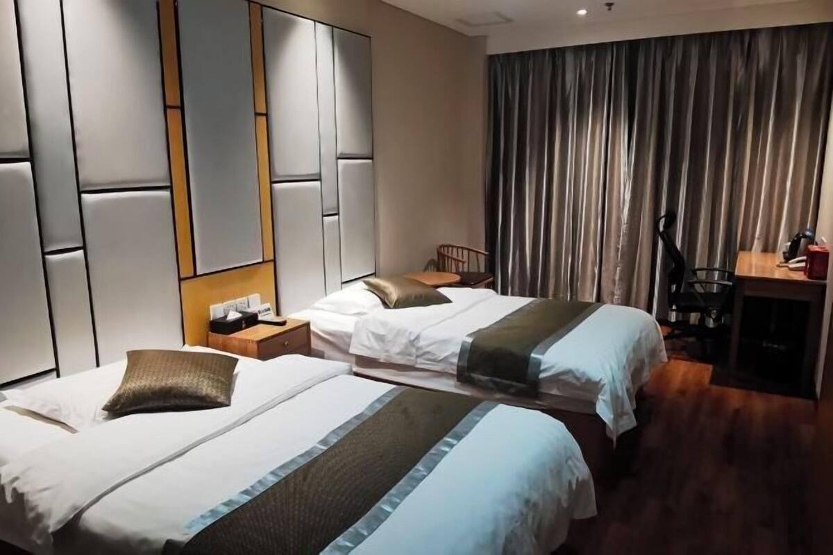 Habitación de hotel con dos camas, un escritorio, una silla y un amplio ventanal con cortinas.
