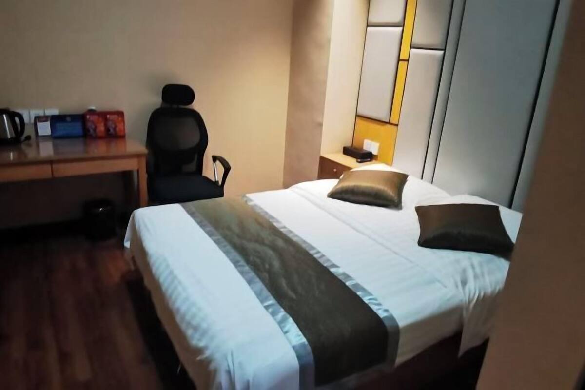 Habitación de hotel con cama, escritorio, silla y mesita de noche con lámpara.