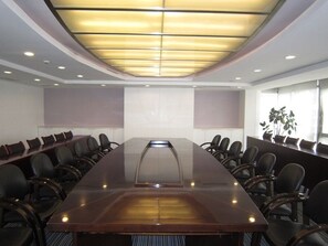 Conference room with a long table and chairs, featuring a large display screen and natural light.