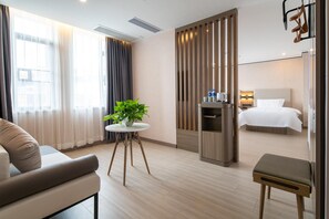 A hotel room with a bed, a seating area with a table and chairs, a plant, and a minibar. - Jin Tai Zi Hotel - Zhuhai (Zhuhai)