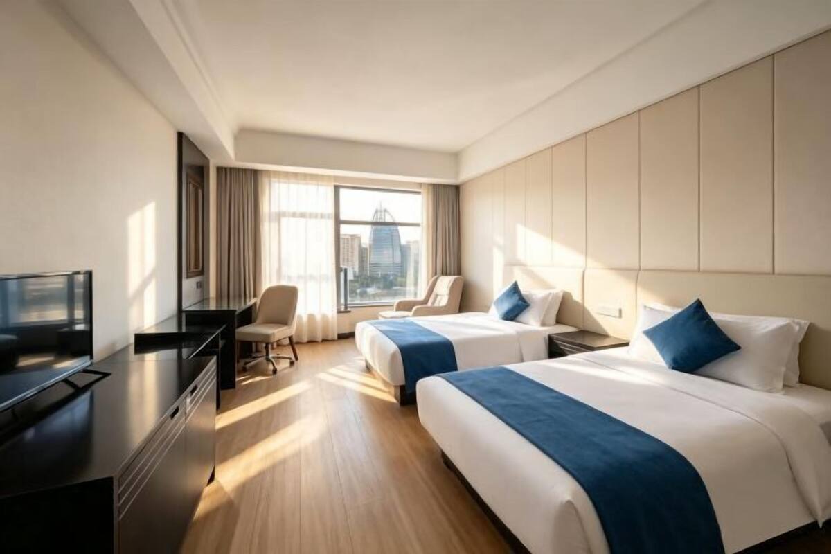A hotel room with two beds, a desk, a chair, and a TV.
