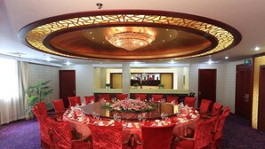 Une salle de conférence avec une table ronde, des chaises rouges et un lustre.