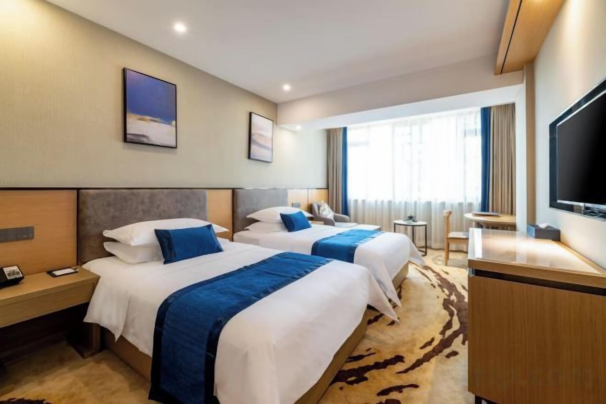 A hotel room with two beds, a desk, a TV, and a window with curtains.