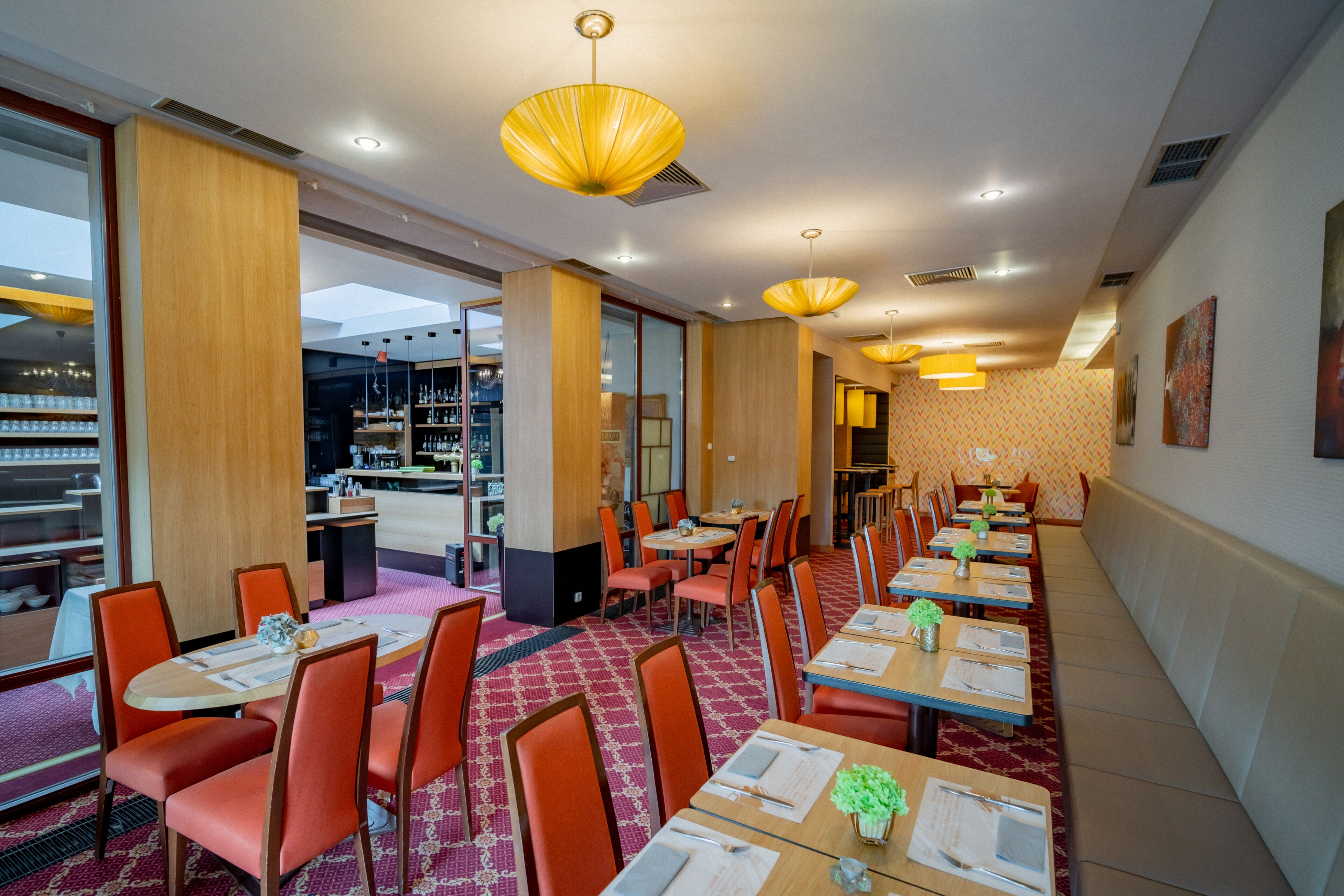 Un restaurant doté de nombreuses tables et chaises, d’un tapis à motifs et d’un éclairage suspendu.