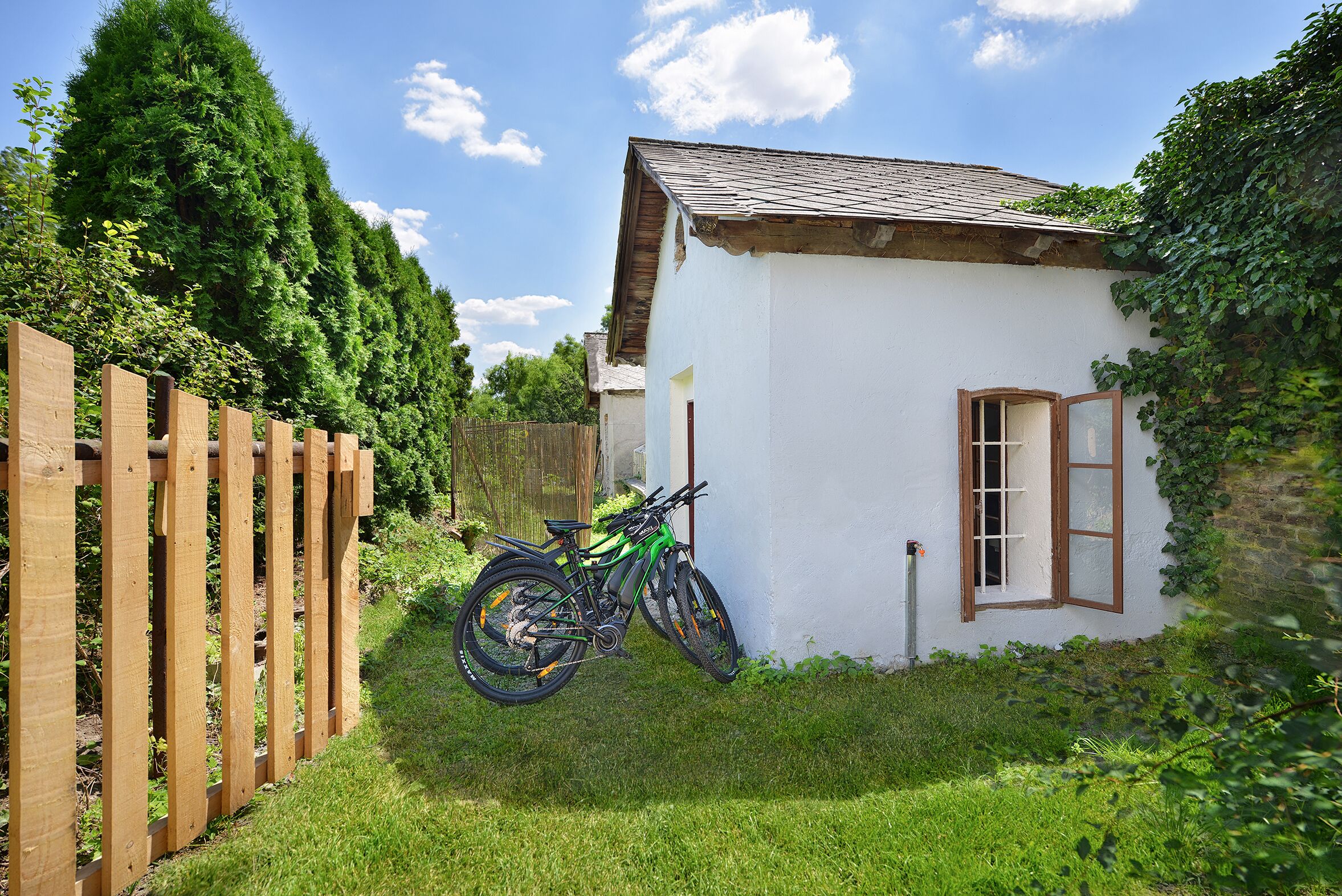 Ein kleines weißes Haus mit Holzzaun, einem Fahrrad und einer Holztür.