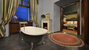 Une salle de bain avec une baignoire sur pieds, une petite cheminée et une vue sur la chambre à coucher par une porte ouverte.