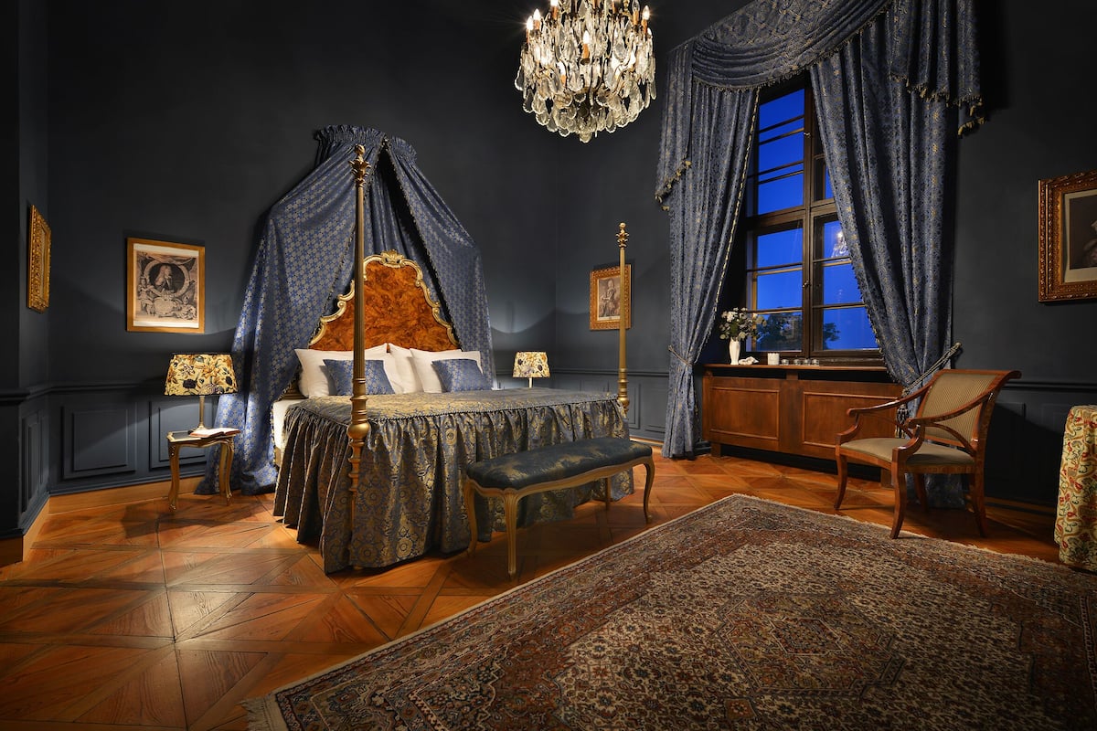 Een slaapkamer met een hemelbed, een kroonluchter en een groot raam met gordijnen.