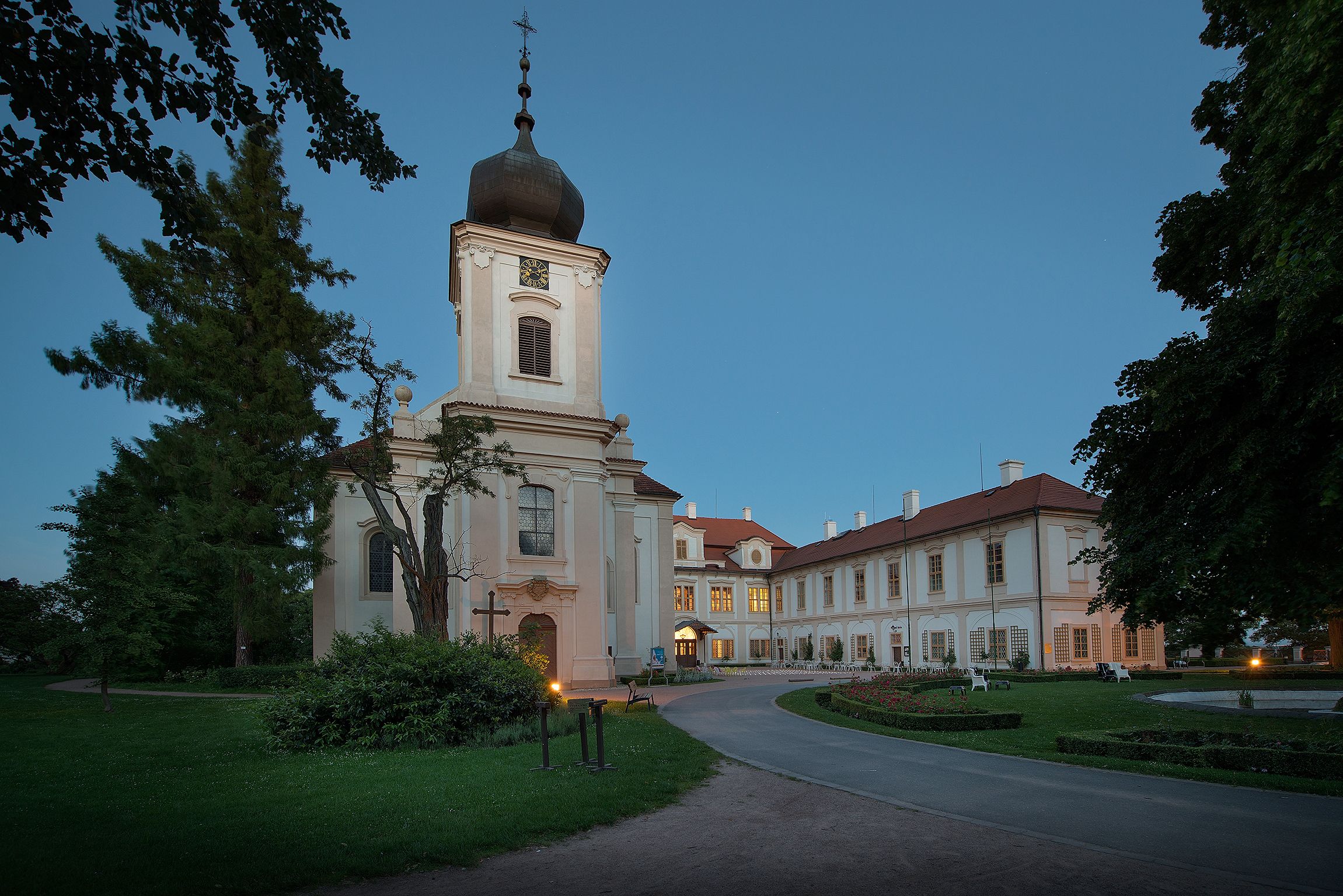 A large, historic building with a prominent tower and a well-maintained garden.