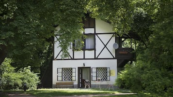 Un edificio tradicional con entramado de madera, con un banco y una mesa afuera, rodeado de árboles.
