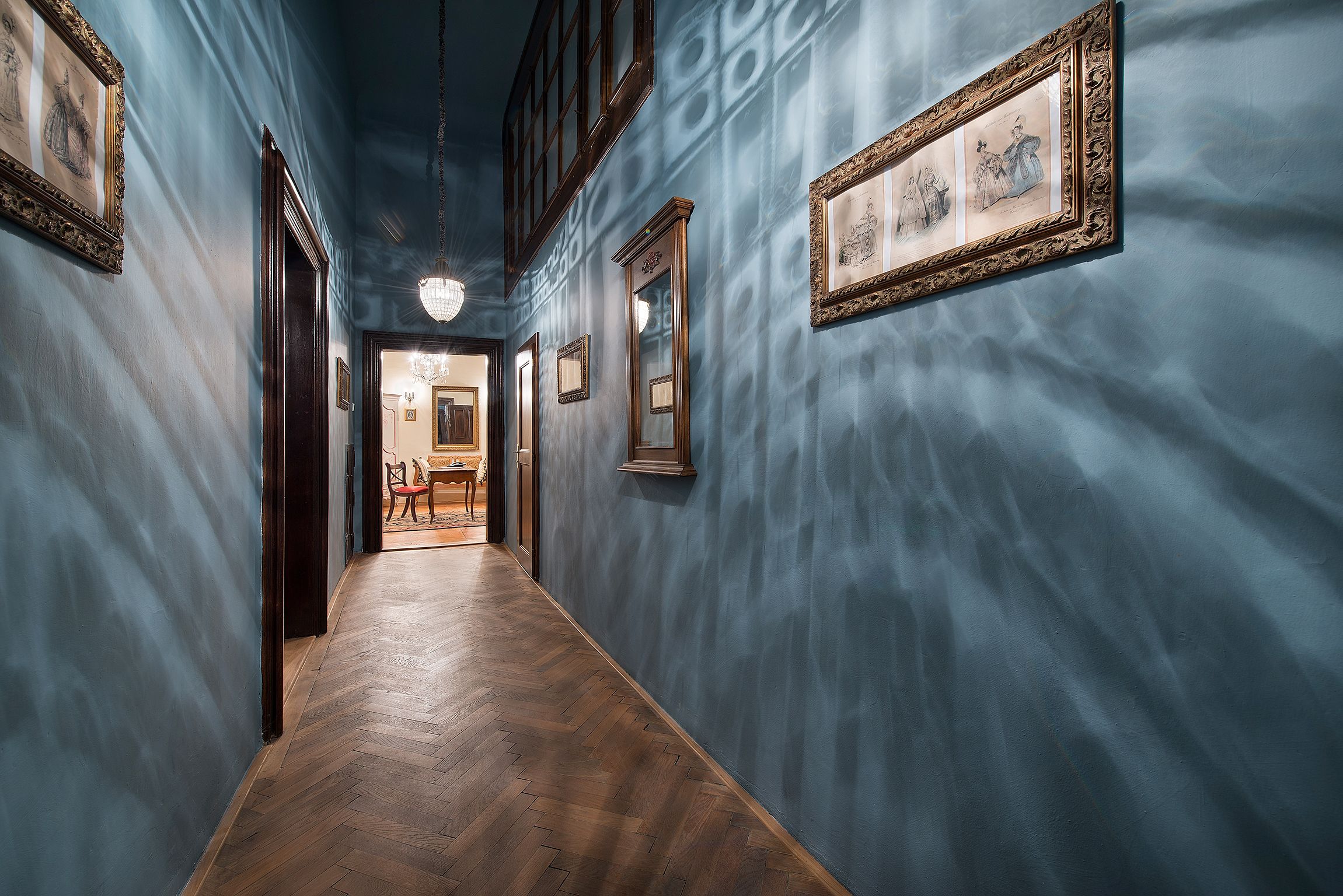 A hallway with blue walls, wooden flooring, and framed artwork.