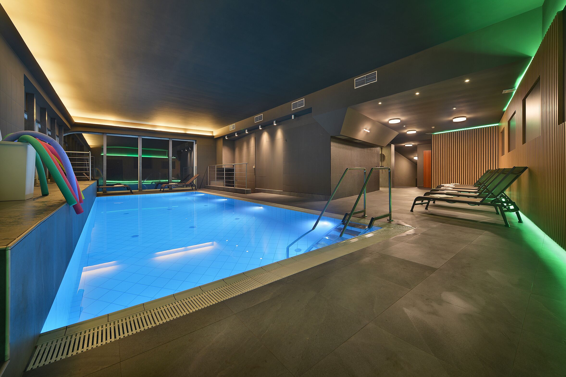 An indoor swimming pool with a clear water surface, surrounded by a tiled floor and walls.