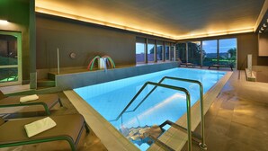Une piscine intérieure aux parois en verre transparent, offrant une vue sur l’extérieur, et dotée d’un design moderne avec un sol carrelé et des rampes en métal.