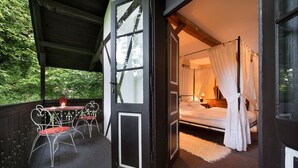 Une terrasse en bois avec une table et des chaises, un lit à baldaquin et une vue sur la verdure.