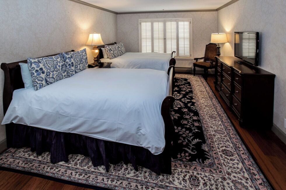 A double bed with a patterned bedspread, a bedside table with a lamp, a chair, a dresser, and a television.