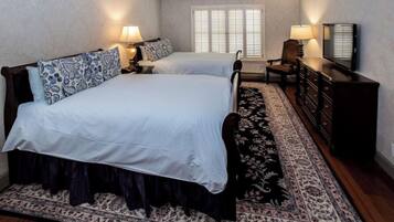 A double bed with a patterned bedspread, a bedside table with a lamp, a chair, a dresser, and a television.