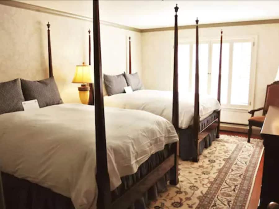 Habitación con cama con dosel, dos camas, una mesita de noche, una lámpara y una silla.