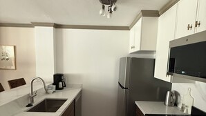 A compact kitchen with a sink, stove, refrigerator, and microwave.