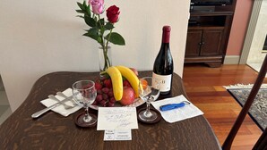 A dining table with a bottle of wine, a vase with roses, and a fruit bowl. There is a receipt and a pen on the table.