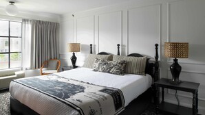 A neatly arranged bedroom with a large bed, two bedside tables with lamps, a chair, and a window with curtains.
