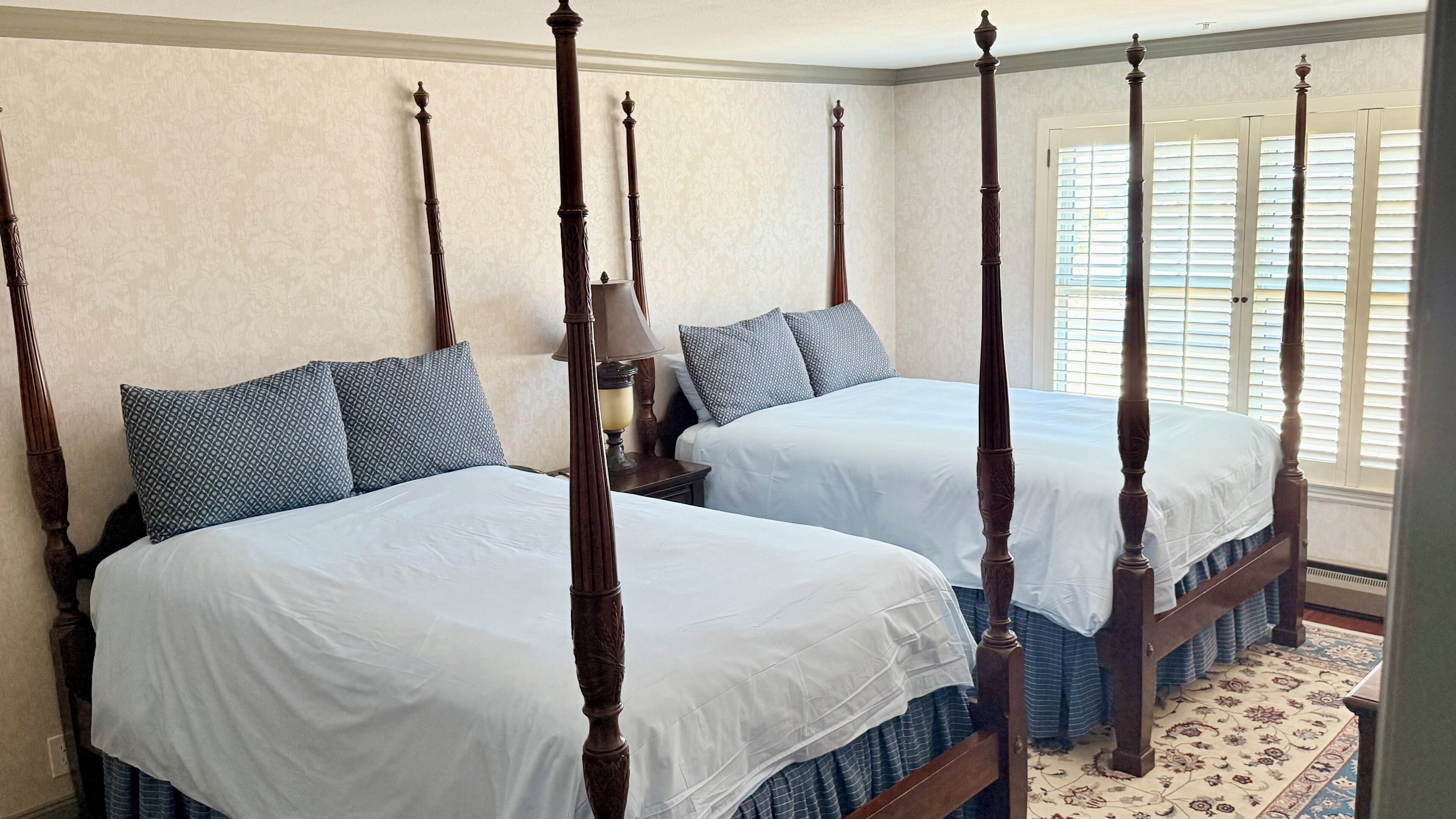 A bedroom with four wooden four-poster beds, a nightstand with a lamp, and a patterned rug.