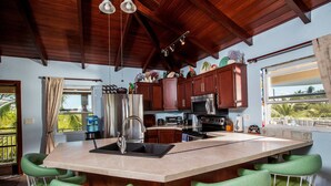 A kitchen with a large island, bar stools, wooden cabinets, and a view of the outdoors. - Casa de Isle (Providenciales)