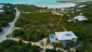 An aerial view of a coastal property with a large house featuring a pool, surrounded by dense tropical vegetation and a clear view of the turquoise sea. - Casa de Isle (Providenciales)