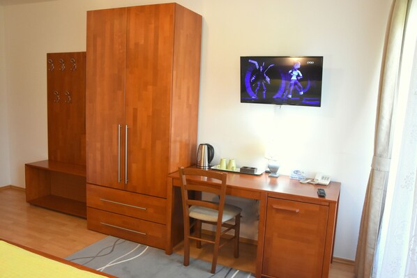 Une pièce comprenant un bureau en bois, une chaise, une armoire et un téléviseur à écran plat fixé au mur.
