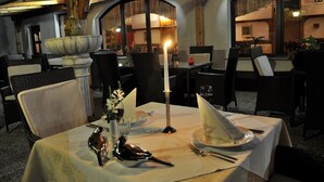 An outdoor dining area with wicker chairs, a table set with a white tablecloth, a candle, and decorative bird figurines. - Nature Hotel Lukanc Bled (Bled)