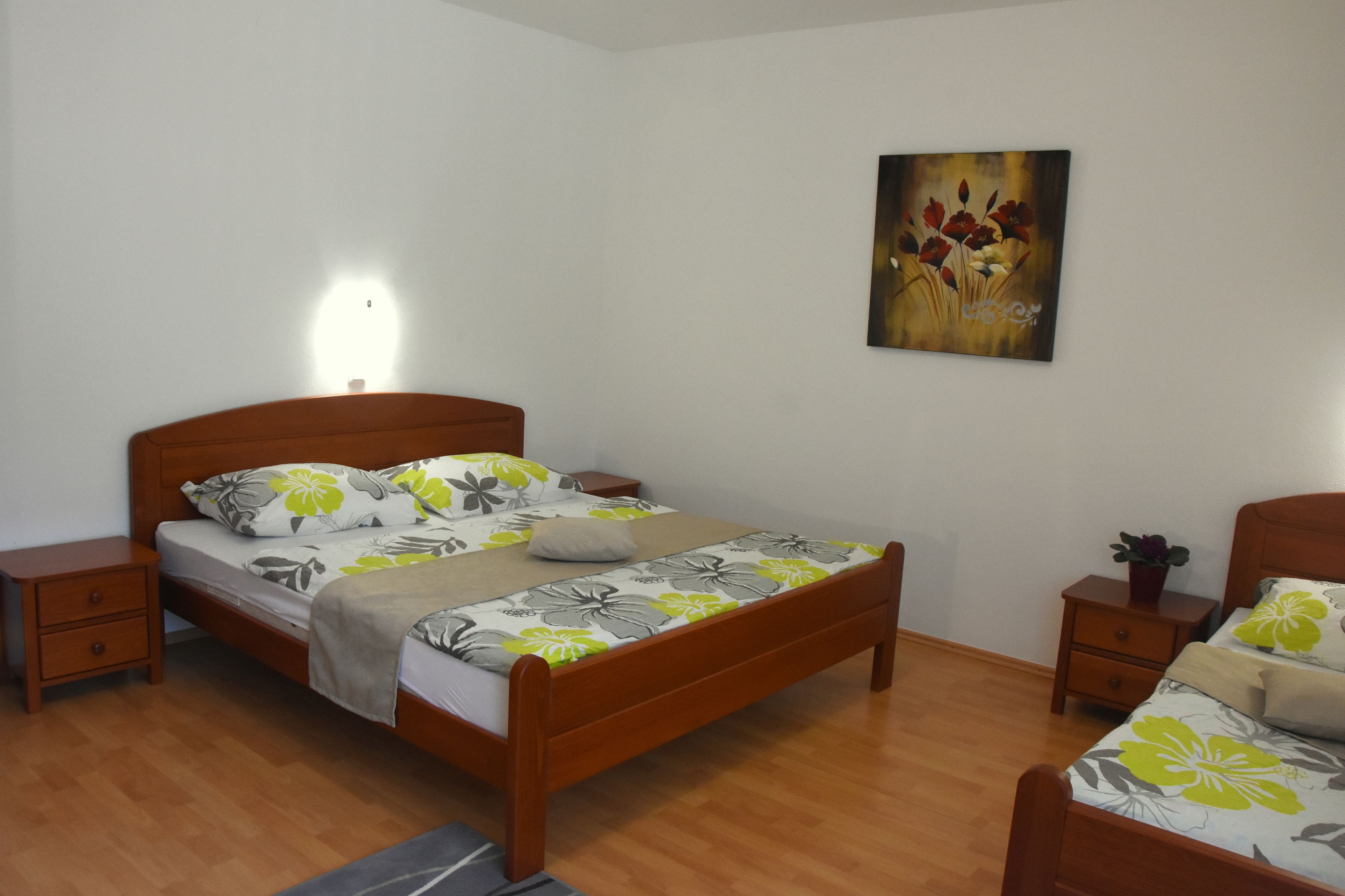 A bedroom with a wooden bed, a nightstand, a bedside table, and a wall-mounted painting.
