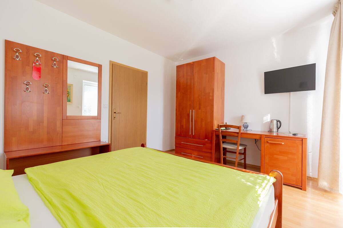 Ein Schlafzimmer mit einem Bett, einem Holzschrank, einem Schreibtisch mit Stuhl und einem an der Wand befestigten Fernseher.