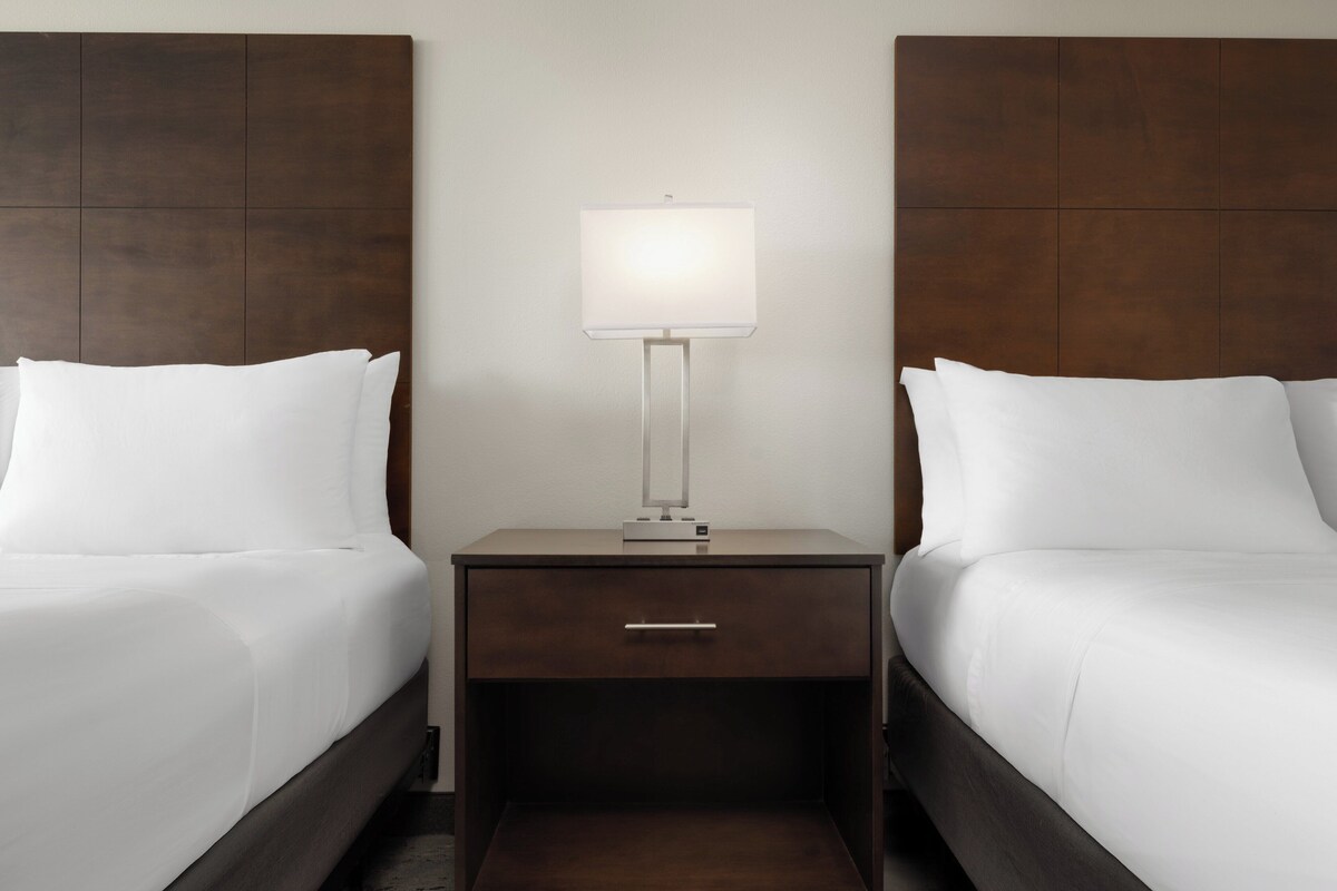 A hotel room with two single beds, a nightstand with a lamp, and a drawer.