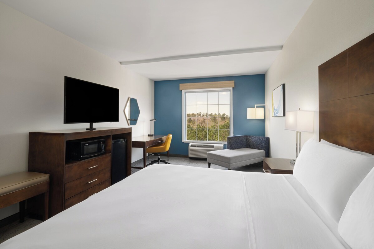 A hotel room with a large bed, a TV, a desk, a chair, a small table, and a window with a view.