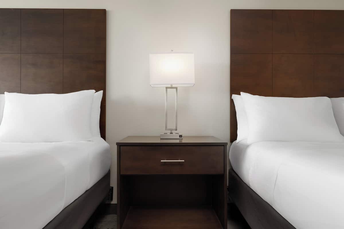 A hotel room with two single beds, a nightstand with a lamp, and a drawer.
