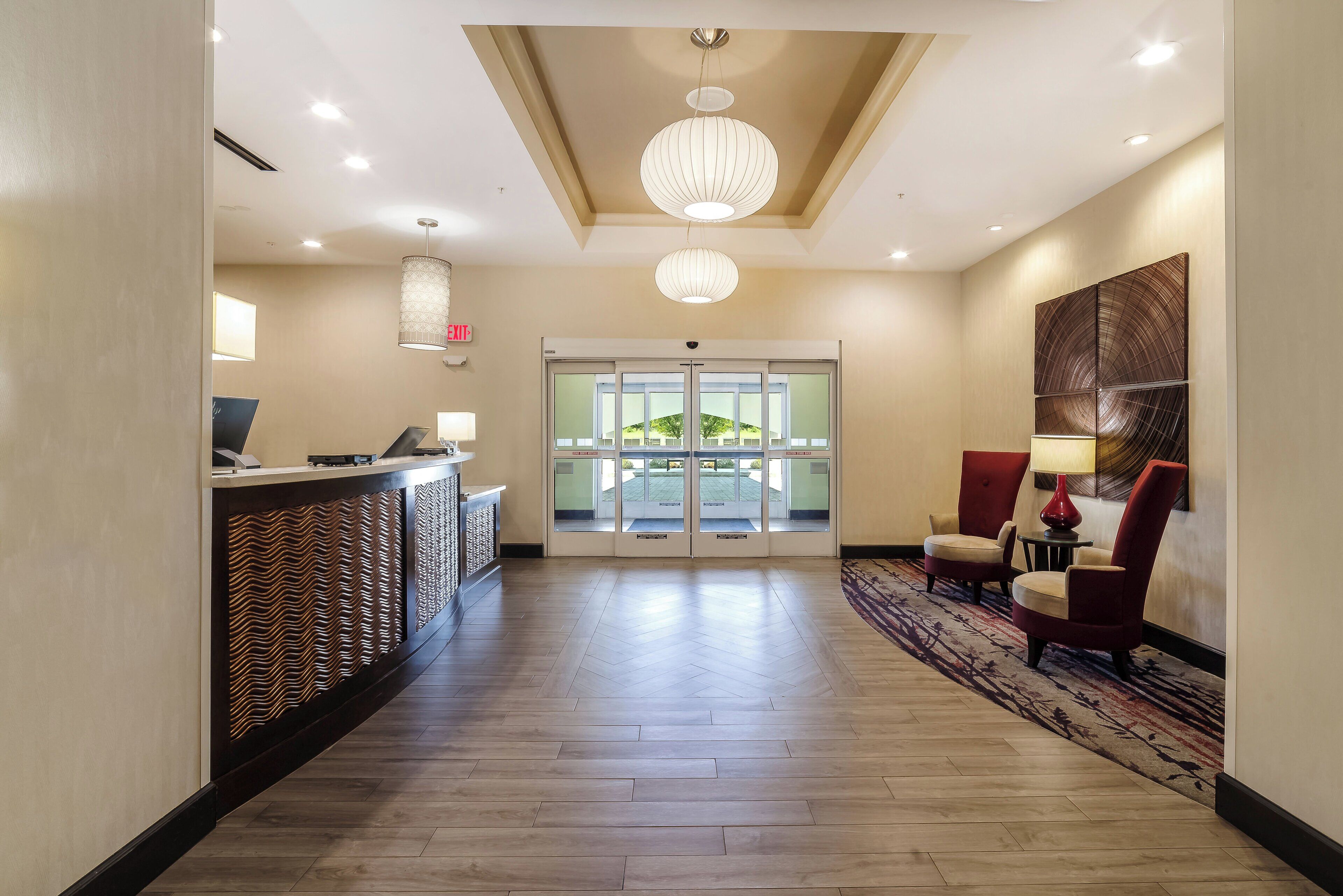 A hotel lobby with a reception desk, a chandelier, a patterned wall, and a carpeted floor.