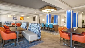 A modern hotel lobby with seating areas, tables, and blue partitions. - Holiday Inn Express & Suites Aiken by IHG (Aiken)