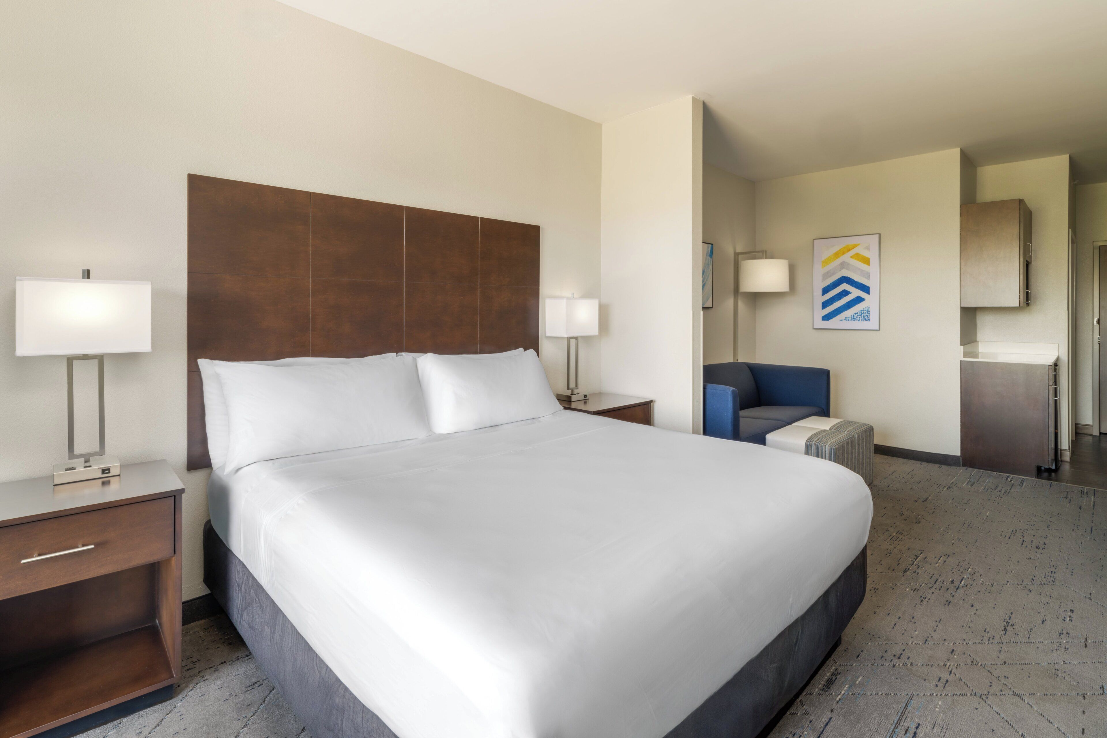 Une chambre d’hôtel avec un grand lit, des tables de chevet avec des lampes, un petit coin salon et une porte donnant sur une autre pièce.