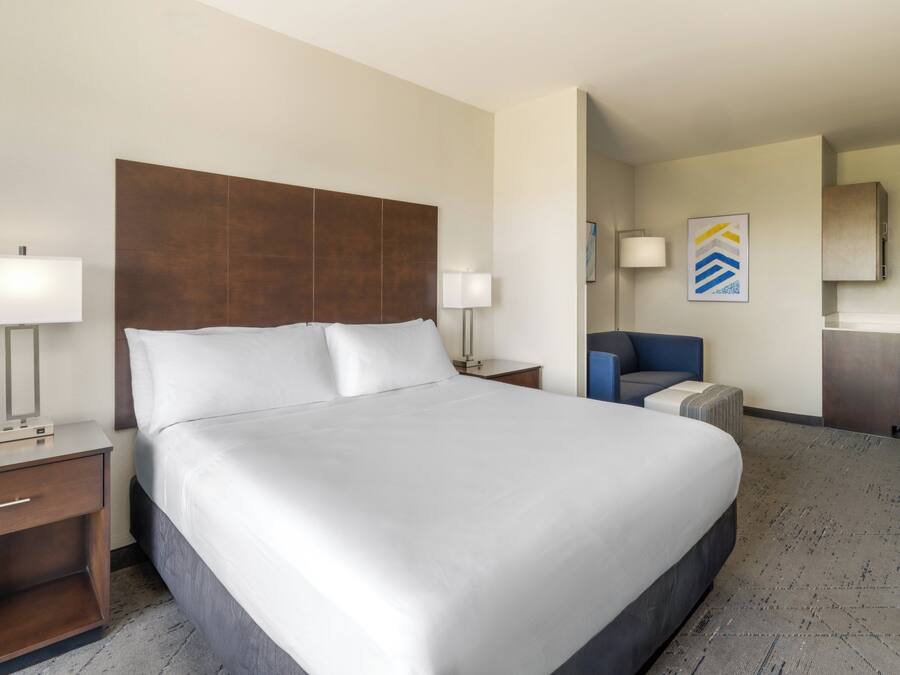 A hotel room with a large bed, bedside tables with lamps, a small seating area, and a door leading to another room.