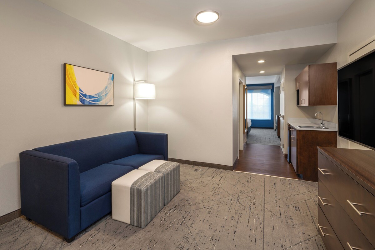 A modern living room with a blue sofa, a white ottoman, a patterned rug, and a painting on the wall.