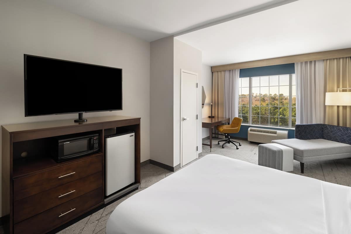 A hotel room with a bed, a TV, a desk with a chair, and a window with curtains.