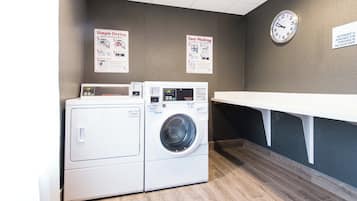 Une buanderie équipée de deux machines à laver, d’un étendoir et de panneaux d’information accrochés au mur.